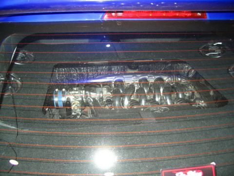 1993 Ford Taurus - A custom intake manifold with a Ford logo is visible through the rear window of a blue vehicle.