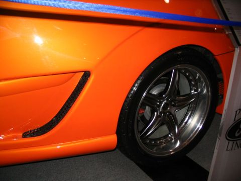 1993 Ford Taurus - Close-up of an orange car's side panel a custom chrome wheel and a black vent insert.