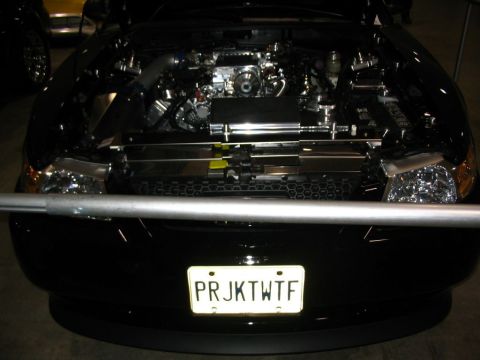 1993 Ford Taurus - Engine bay of a black car, chrome components and a custom license plate reading 'PRJKTWFT'.