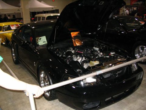 1993 Ford Taurus - A black coupe with its hood open, displaying the engine and chrome wheels at a car show.