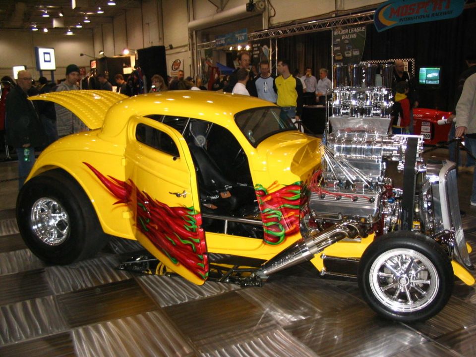 Yellow custom hot rod with flames on doors and a large chrome engine exposed