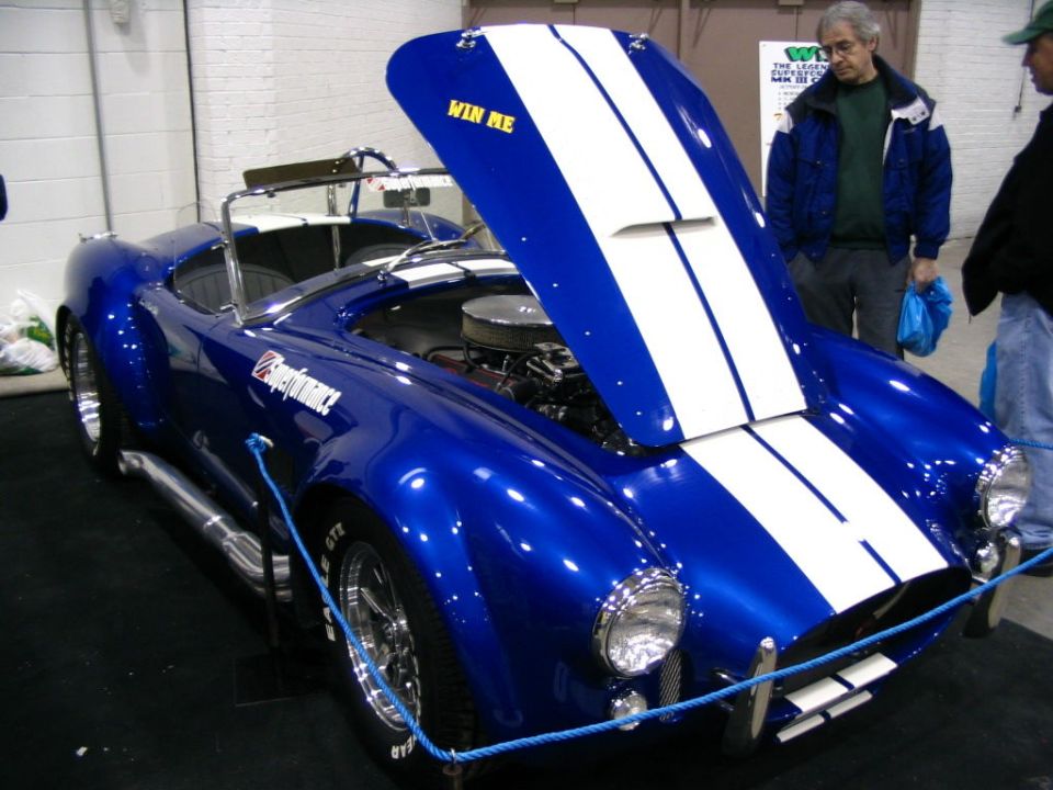 Blue convertible with white racing stripes, hood open, showing engine. Text 'WIN ME' on hood