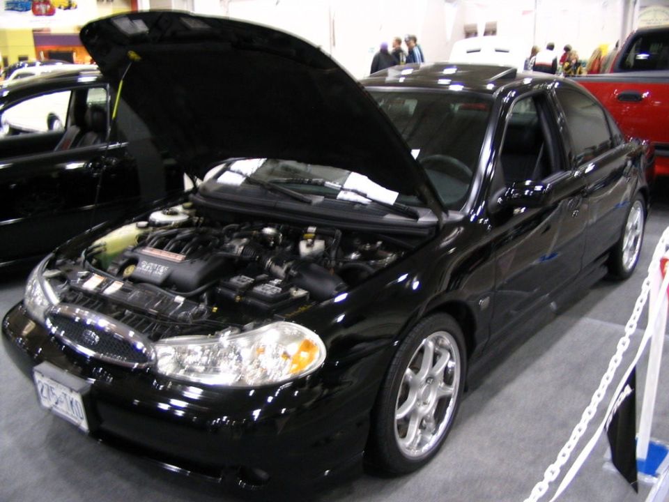 Black sedan with hood open, showing engine. Another black car is to the left, red truck to the right