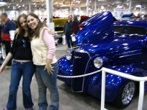1993 Ford Taurus - Two women stand next to a custom hot rod with a vibrant blue paint job and flame details at an indoor car show.