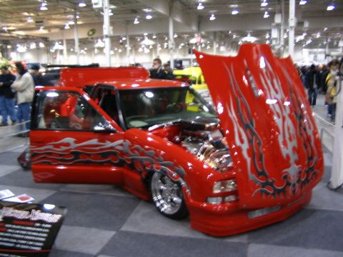 1993 Ford Taurus - Customized red pickup truck displayed indoors with flames painted on the body and hood.