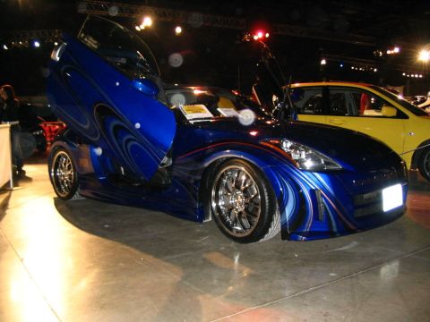 1993 Ford Taurus - A custom blue car with butterfly doors and unique paintwork is displayed at a show, with a yellow car visible in the background.