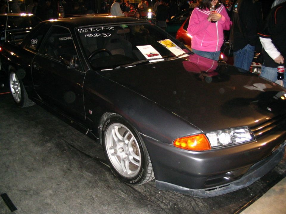 Dark grey coupe with aftermarket wheels and racing seats visible through the window. Text on windshield reads '1/20 EV-X BNR32'