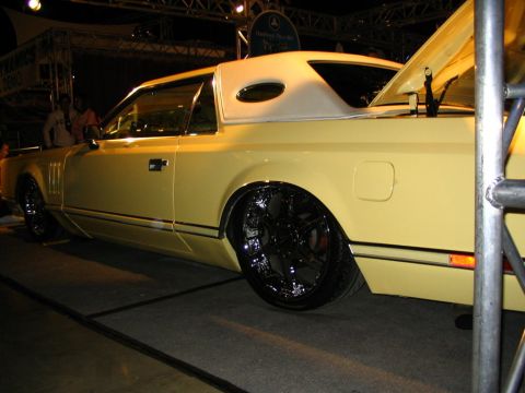 1993 Ford Taurus - Customized yellow coupe with vinyl top and large chrome wheels sits on display.
