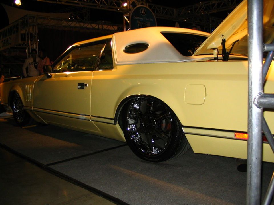 Yellow coupe with vinyl top and large chrome wheels, trunk open