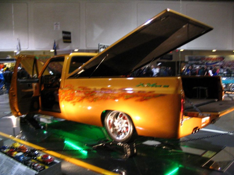 Orange pickup truck with custom flames and open tonneau cover, green underglow, and chrome wheels