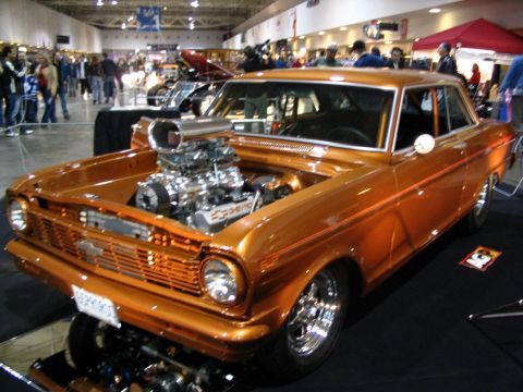 1993 Ford Taurus - This custom orange hot rod features a prominent supercharger and exposed engine, displayed indoors at a car show.