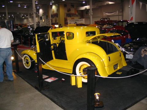 1993 Ford Taurus - A bright yellow coupe hot rod is showcased indoors with its doors open, surrounded by other vehicles.