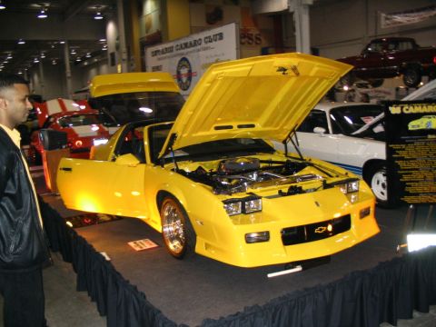 1993 Ford Taurus - A bright yellow sports car, likely a Chevrolet Camaro from the 1980s, is displayed with its hood and driver's door open.