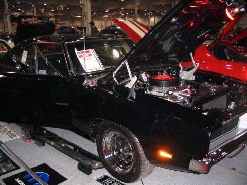 1993 Ford Taurus - A black 1969 Dodge Charger is displayed with its hood open, revealing the engine. Another car with red and white stripes is visible behind…