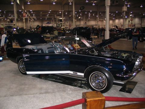 1993 Ford Taurus - A dark blue convertible with white racing stripes is displayed with its hood open at a car show.