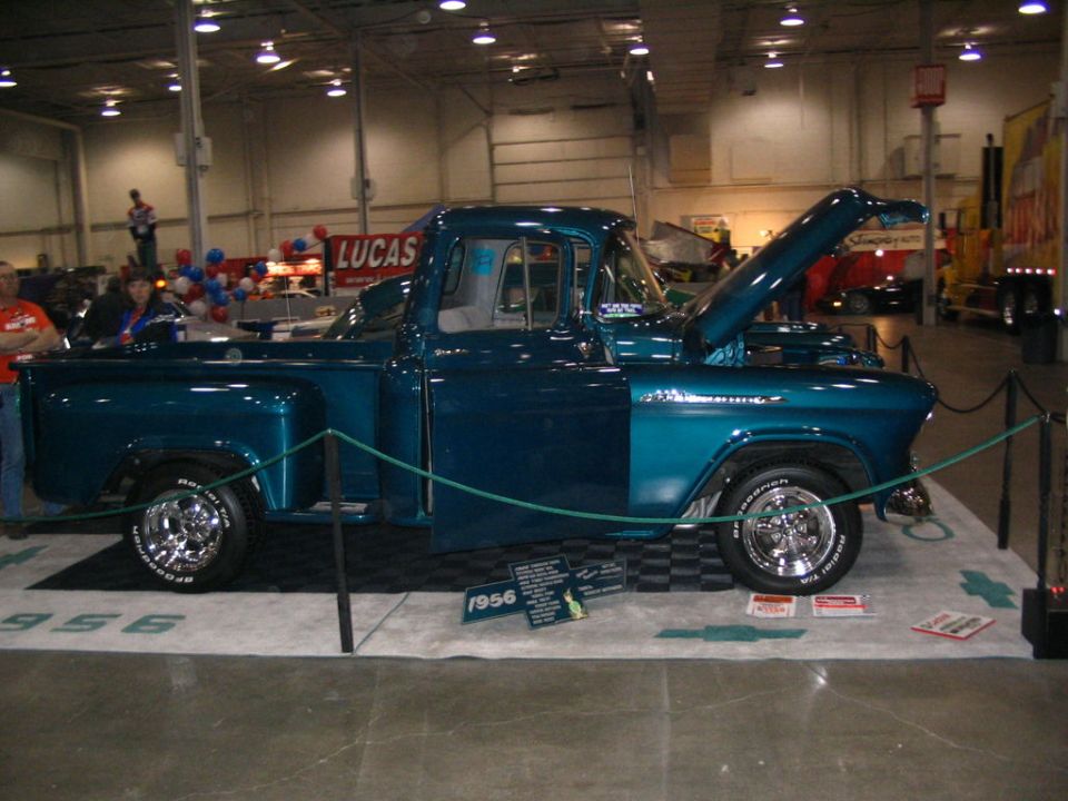 Teal 1956 pickup truck with hood open, side view, chrome wheels, on display