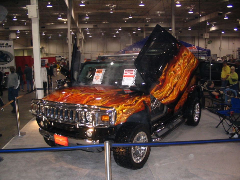 Customized SUV with flame graphics and upward-opening doors, displayed indoors