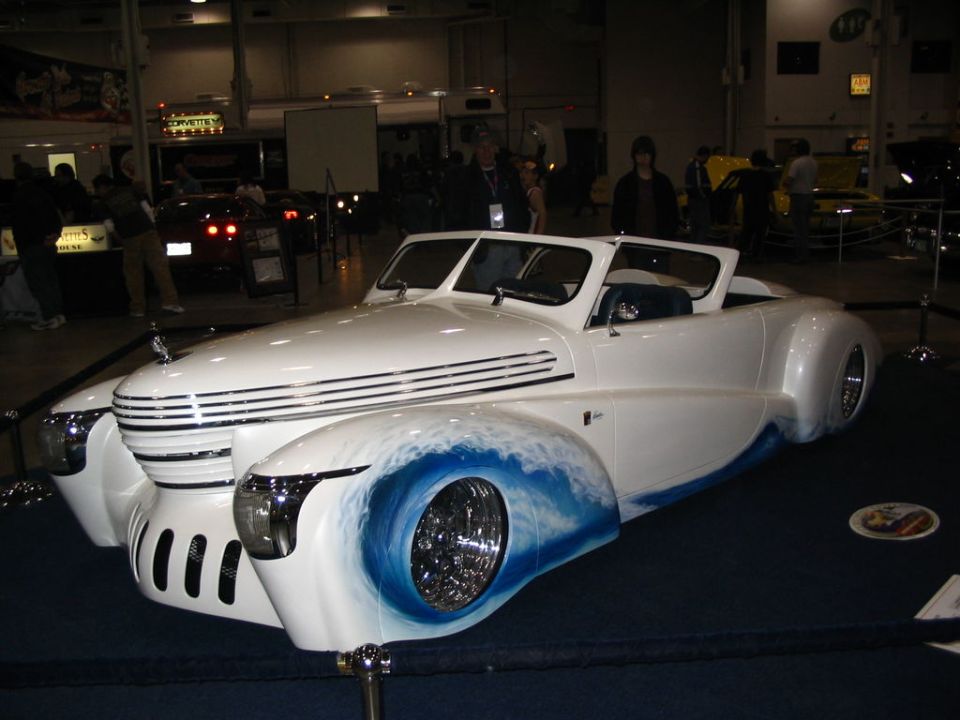 Custom hot rod with white body, blue wave graphics on front fenders, and chrome wheels