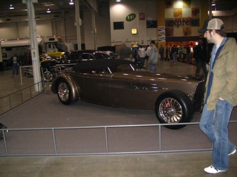 1993 Ford Taurus - A custom hot rod is showcased indoors at an event, with a spectator looking on.