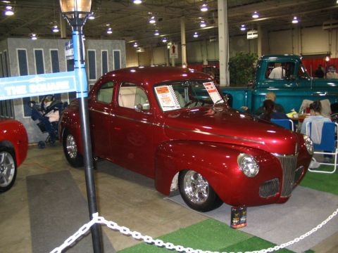 1993 Ford Taurus - A classic red Ford coupe is displayed indoors next to a teal pickup truck, with a street sign prop nearby.
