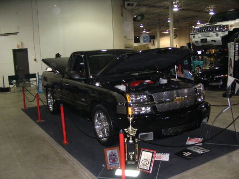 1993 Ford Taurus - A black Chevrolet pickup truck is displayed indoors with its hood open, trophies in front.