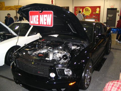 1993 Ford Taurus - Black car with hood open at a show, displaying its modified engine and turbocharger. Another vehicle is visible to the left.