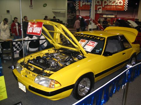 1993 Ford Taurus - A yellow 1987 Ford Mustang coupe is displayed with its hood open, revealing the engine and interior details.