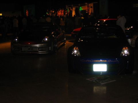 1993 Ford Taurus - Two sports cars are displayed indoors at night, with one custom text on its front bumper.