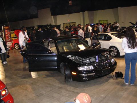 1993 Ford Taurus - A black sedan is displayed with its hood and doors open at an indoor car event.