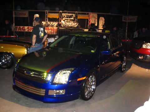 1993 Ford Taurus - Customized blue Ford sedan at an event, with other vehicles visible.