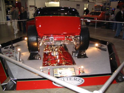 1993 Ford Taurus - Custom red hot rod displayed with intricate chrome suspension and oversized rear tires. A sign indicates 'BUTTERZ'.