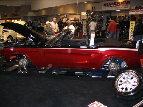 1993 Ford Taurus - Classic red convertible on display at an auto show, with its hood up and wheels removed.