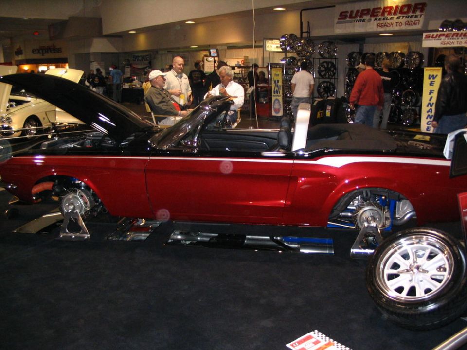 Red convertible classic car with hood open, on display stands, showing suspension