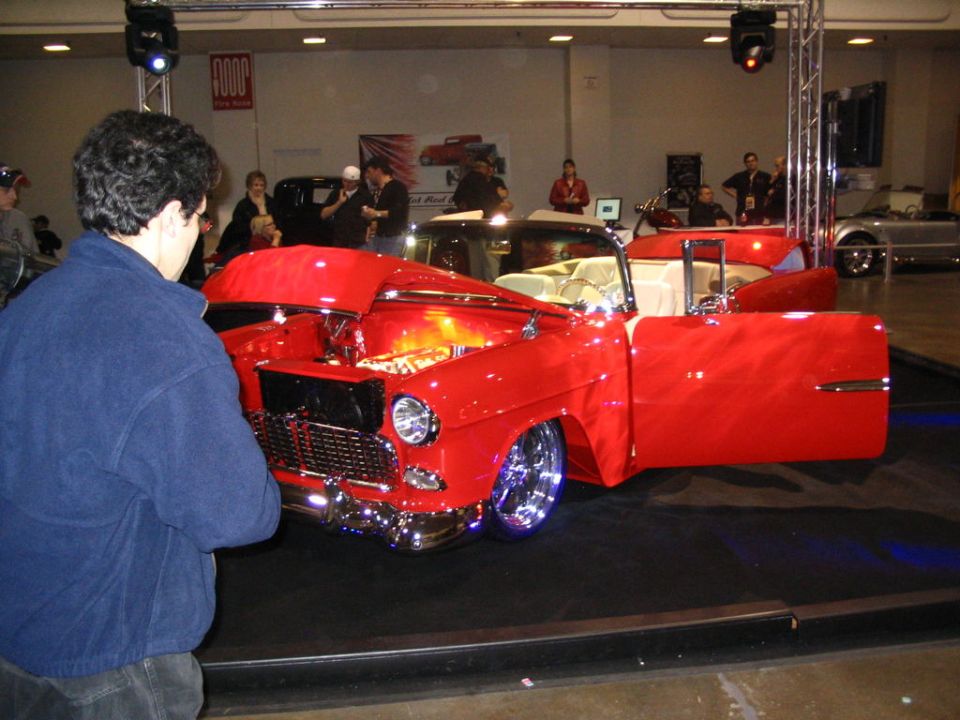 Red 1955 Chevrolet Bel Air convertible hot rod on display, hood and driver's door open. Chrome wheels and interior visible