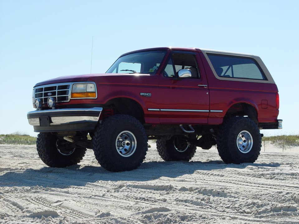 Red 1992 Ford Bronco with body lift and large tires on sand