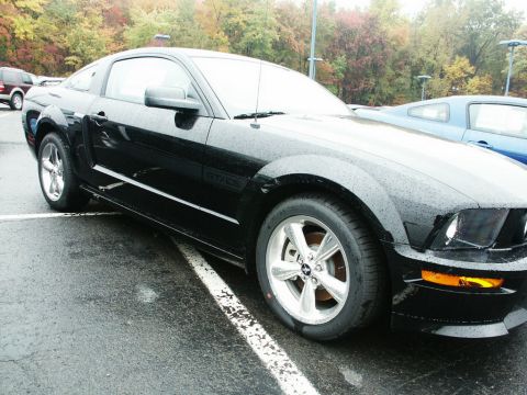2001 Mercury Grand Marquis - Black Ford Mustang GT with chrome wheels, parked outdoors on a wet day.