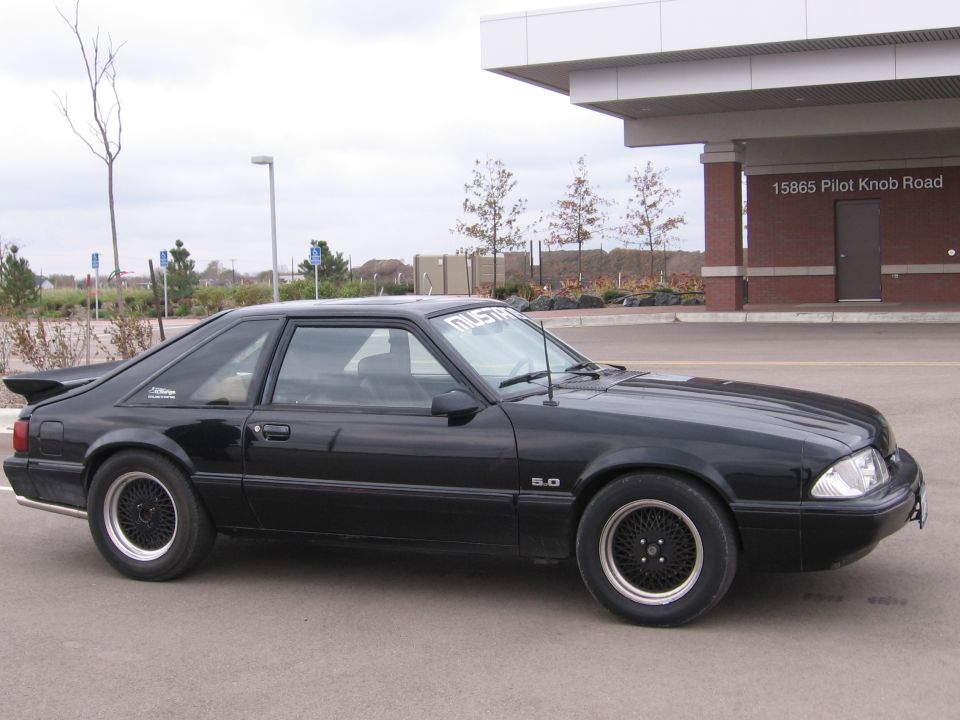 Black Fox-body Mustang LX 5.0 hatchback side view on black lace wheels in a parking lot