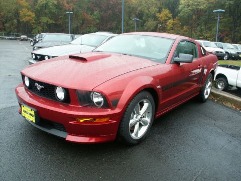 2001 Mercury Grand Marquis - A red Ford Mustang is parked in a lot on a rainy day. The car has a hood scoop and racing stripes.