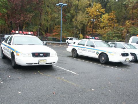 2001 Mercury Grand Marquis - Two white police cars are parked in a lot with autumn trees in the background.