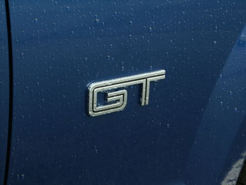 2001 Mercury Grand Marquis - A close-up of a chrome GT emblem on a blue vehicle's fender, showing water droplets on the paint.