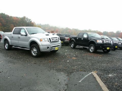 2001 Mercury Grand Marquis - Two Ford F-150 pickup trucks are parked on a gravel lot with other vehicles in the background.