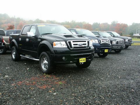 2001 Mercury Grand Marquis - Several Ford F-150 pickup trucks are lined up in a dealership lot under an overcast sky.