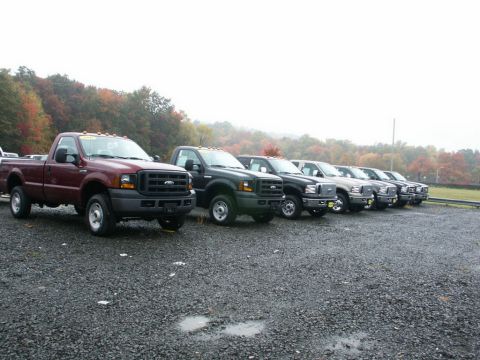2001 Mercury Grand Marquis - A line of Ford F-250 trucks are parked on a gravel lot with autumn trees in the background.