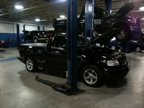 2001 Mercury Grand Marquis - A black Ford F-150 Lightning pickup truck is serviced in a garage bay, with other vehicles present.