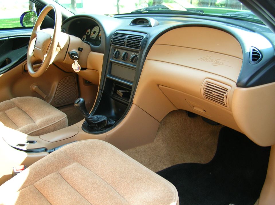 Interior of a 1995 Ford Mustang, showing tan seats, dashboard, and center console with a manual shifter