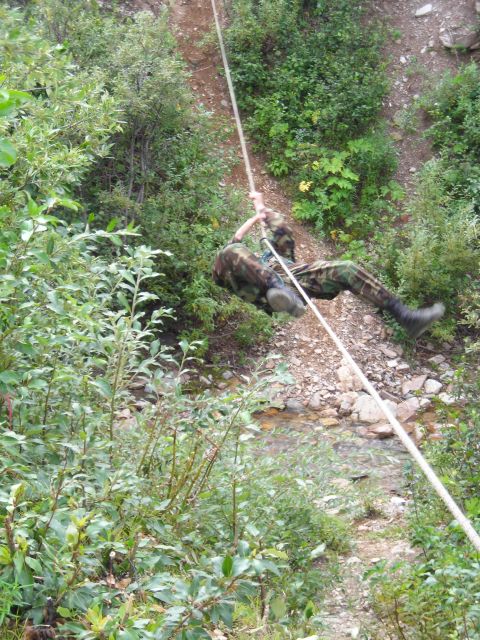 2003 Jeep TJ - A person descends a steep, vegetated incline using a rope, with a stream visible below.