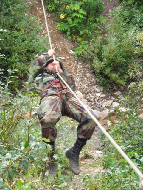 2003 Jeep TJ - A person in camouflage gear rappels down a steep, vegetated slope using a thick rope.