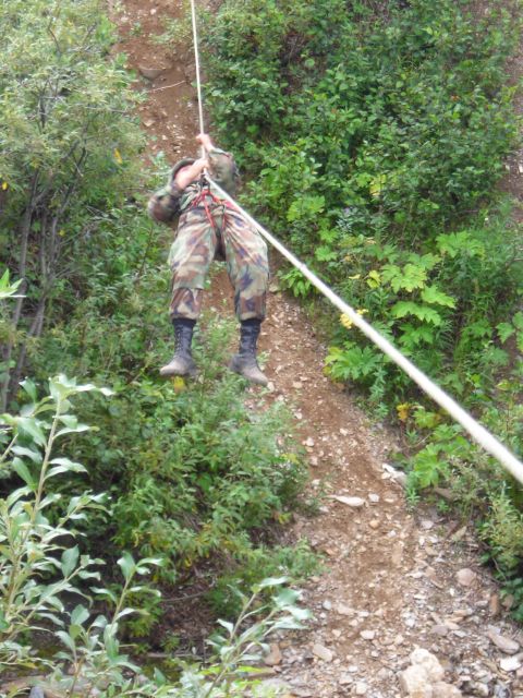 2003 Jeep TJ - A person in camouflage gear is rappelling down a steep, vegetated slope using a rope.