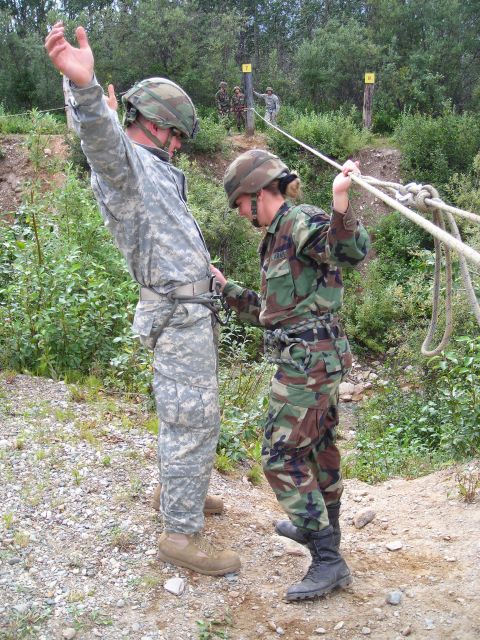 2003 Jeep TJ - Two soldiers participate in a rope training exercise on an outdoor course with trees and obstacles in the background.