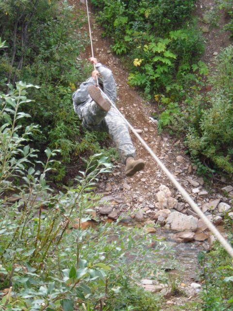 2003 Jeep TJ - A soldier descends a steep, vegetated incline using a rope, with a shallow stream flowing below.
